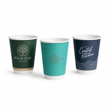 Load image into Gallery viewer, Three double walled custom branded hot cups on a white background: a dark green Wild Oak Coffee cup with a gold tree logo, a teal Port of Mocha cup with a gold ornamental design, and a navy The Coastal Kitchen cup with white script and wave graphics.