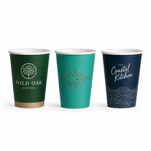 Load image into Gallery viewer, Three single walled paper coffee cups on a white background: a dark green cup with a gold band and 'Wild Oak Coffee' logo, a teal cup with 'Port of Muca' text, and a dark navy cup with 'The Coastal Kitchen' script and wave pattern.