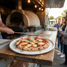 Load image into Gallery viewer, Wood-fired pizza being served on a biodegradable pizza plate at an outdoor event with a pizza truck in the background.