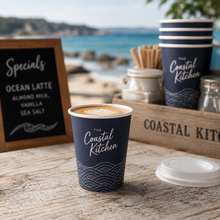 Load image into Gallery viewer, Single walled express custom branded hot cup on a cafe table next to the beach and other additional catering items. 
